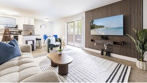 A modern living room with a flat-screen TV, a sofa, a coffee table, and a dining area with a blue tablecloth.