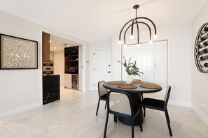 A dining area with a round table, black chairs, a vase with greenery, and a modern pendant light.