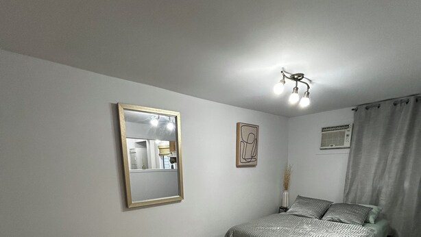 A bedroom with a bed, a chair, a mirror, and a window with curtains. - Charming, cozy studio 7 minutes from Ottawa (Gatineau)