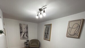 A bedroom with a bed, a chair, a desk, and two wall-mounted artworks. - Charming, cozy studio 7 minutes from Ottawa (Gatineau)