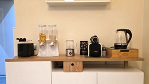 Et tekøkken med kaffemaskine, elkedel, blender og kaffekværn på en træbordplade.