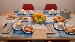 Et spisebord dækket med croissanter, kaffe og en frugtkurv.
