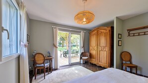 Ein Schlafzimmer mit einem großen Bett, einem Holzschrank, einem Stuhl, einem Tisch und Blick ins Freie durch eine Schiebetür.