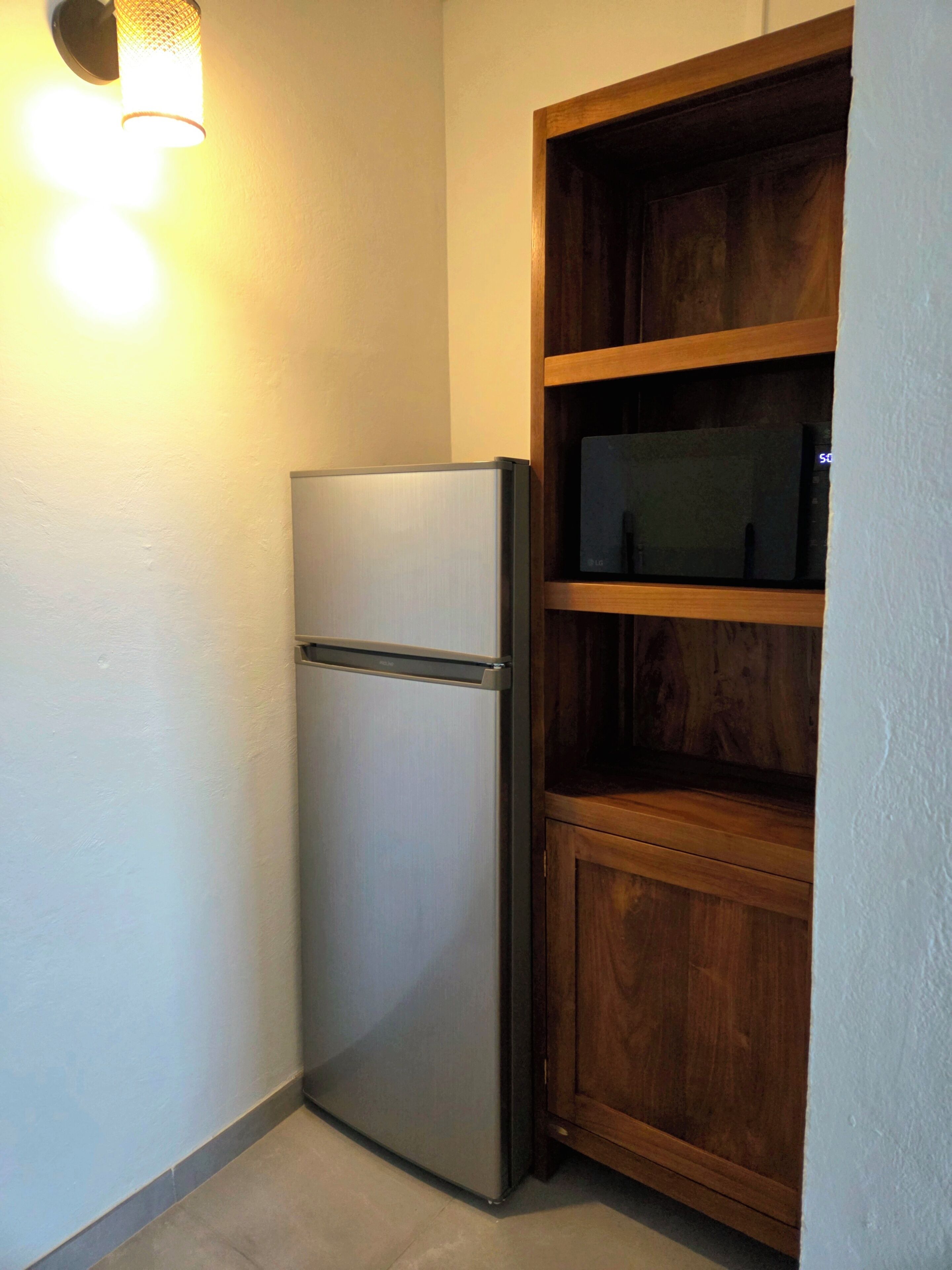 Une cuisine compacte dotée d’un réfrigérateur encastré, d’étagères en bois et d’un luminaire fixé au mur.