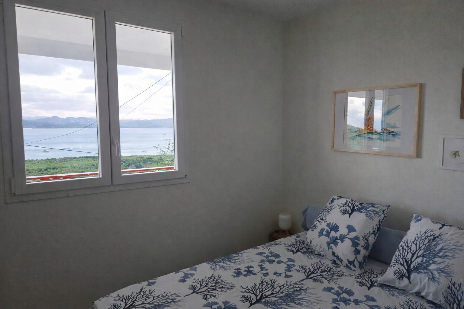 Una camera da letto con un letto, una finestra vista mare e un quadro appeso al muro.