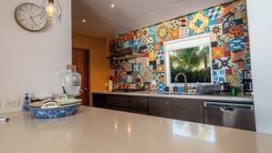Uma cozinha com painel de azulejos coloridos, luminária moderna e máquina de lavar louça embutida.