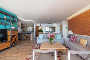 A modern living room with a sofa, coffee table, TV, and a kitchen in the background. - Ocean bliss, infinity pool, beach front, inhouse restaurant, with parking. (Puerto Vallarta)