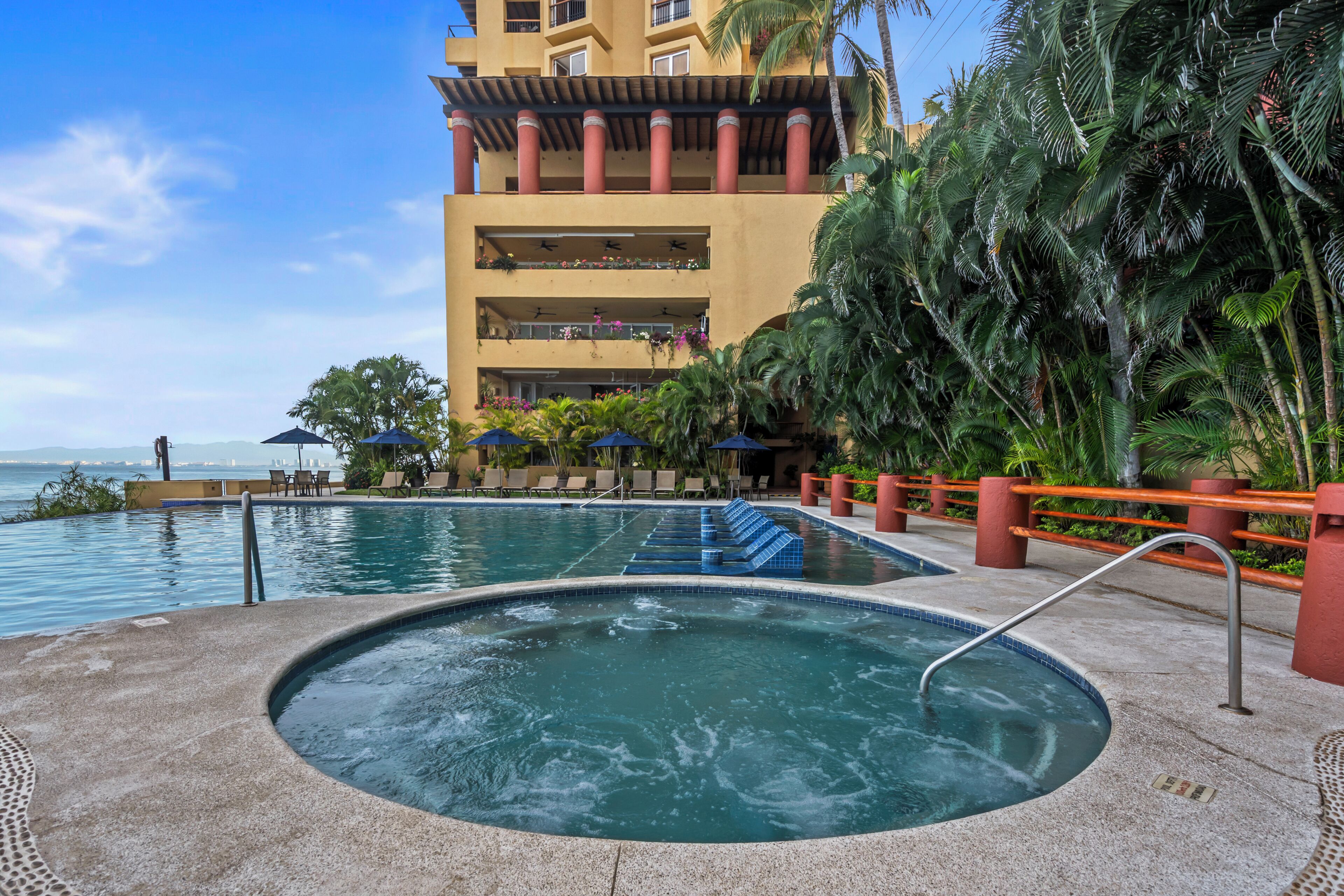 A pool area with a hot tub, lounge chairs, and a view of the ocean.