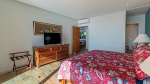 Quarto com cama, televisão, penteadeira e porta que dá para outro espaço.