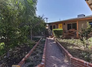 A pathway leading to a building with a yellow door, surrounded by greenery and a brick border. - Private Dream Home with Pool in LA (Los Angeles)