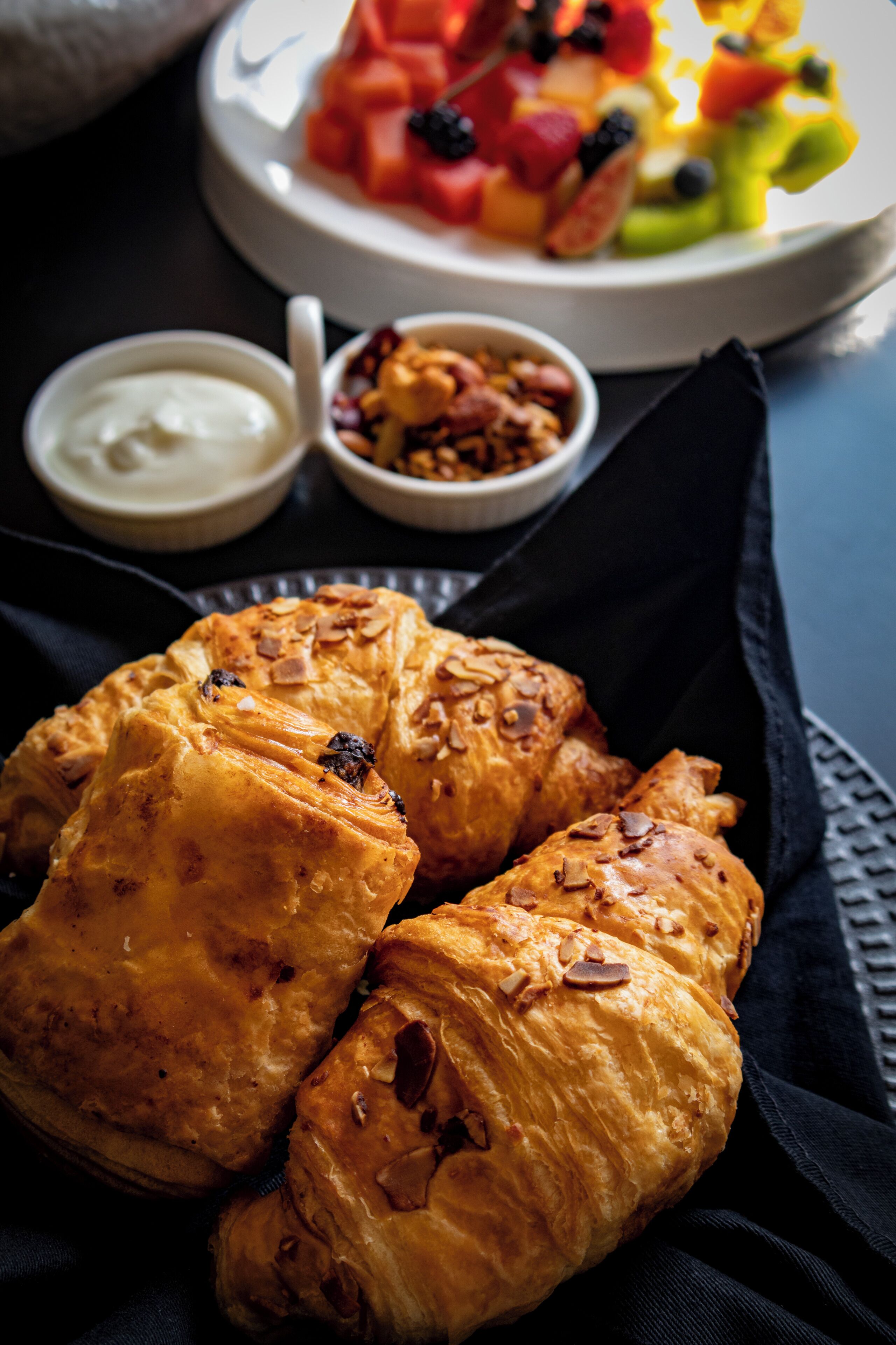 A plate of pastries with a side of fruit salad and a small bowl of nuts.