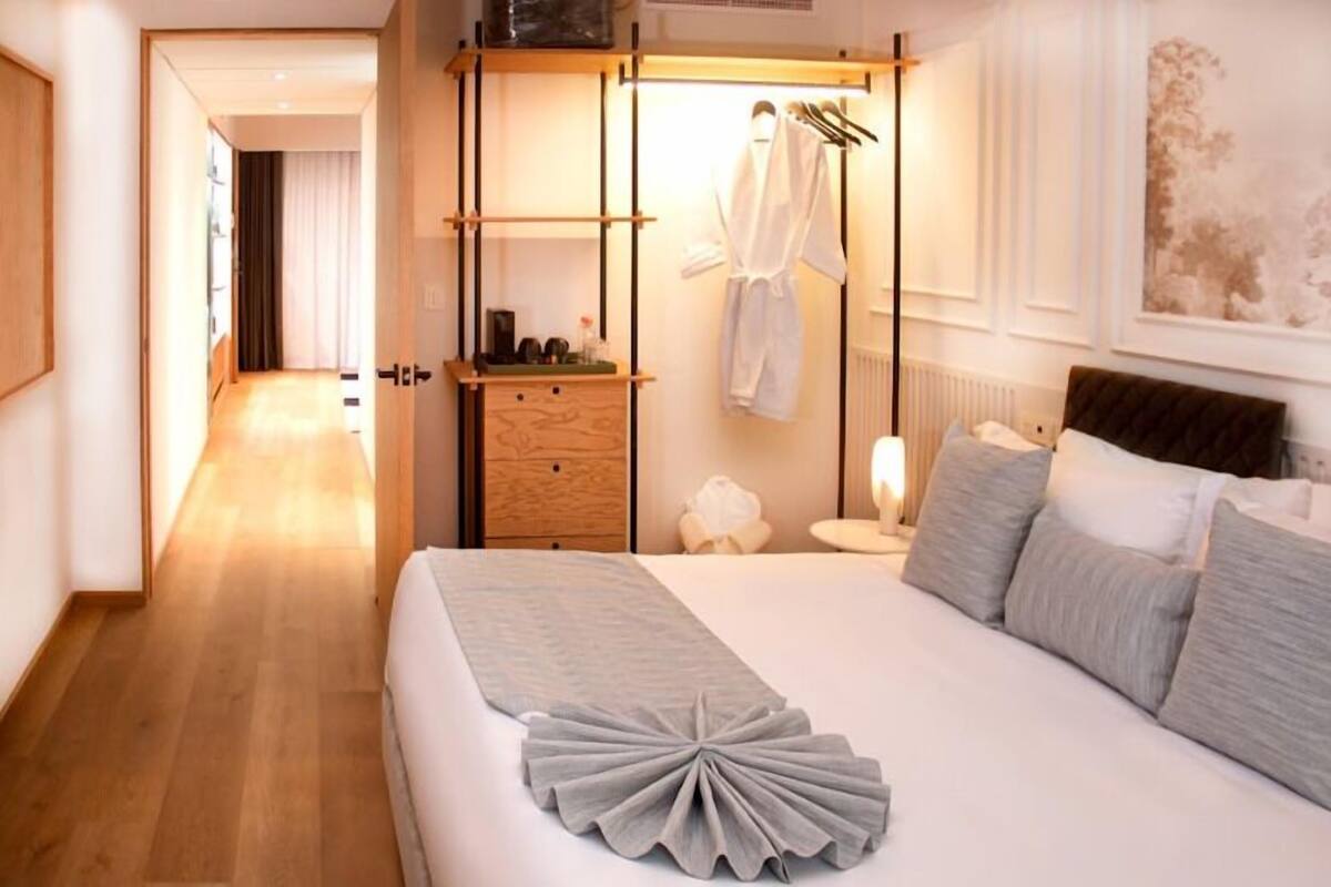 Quarto de hotel com cama, mesa de cabeceira, luminária e armário.