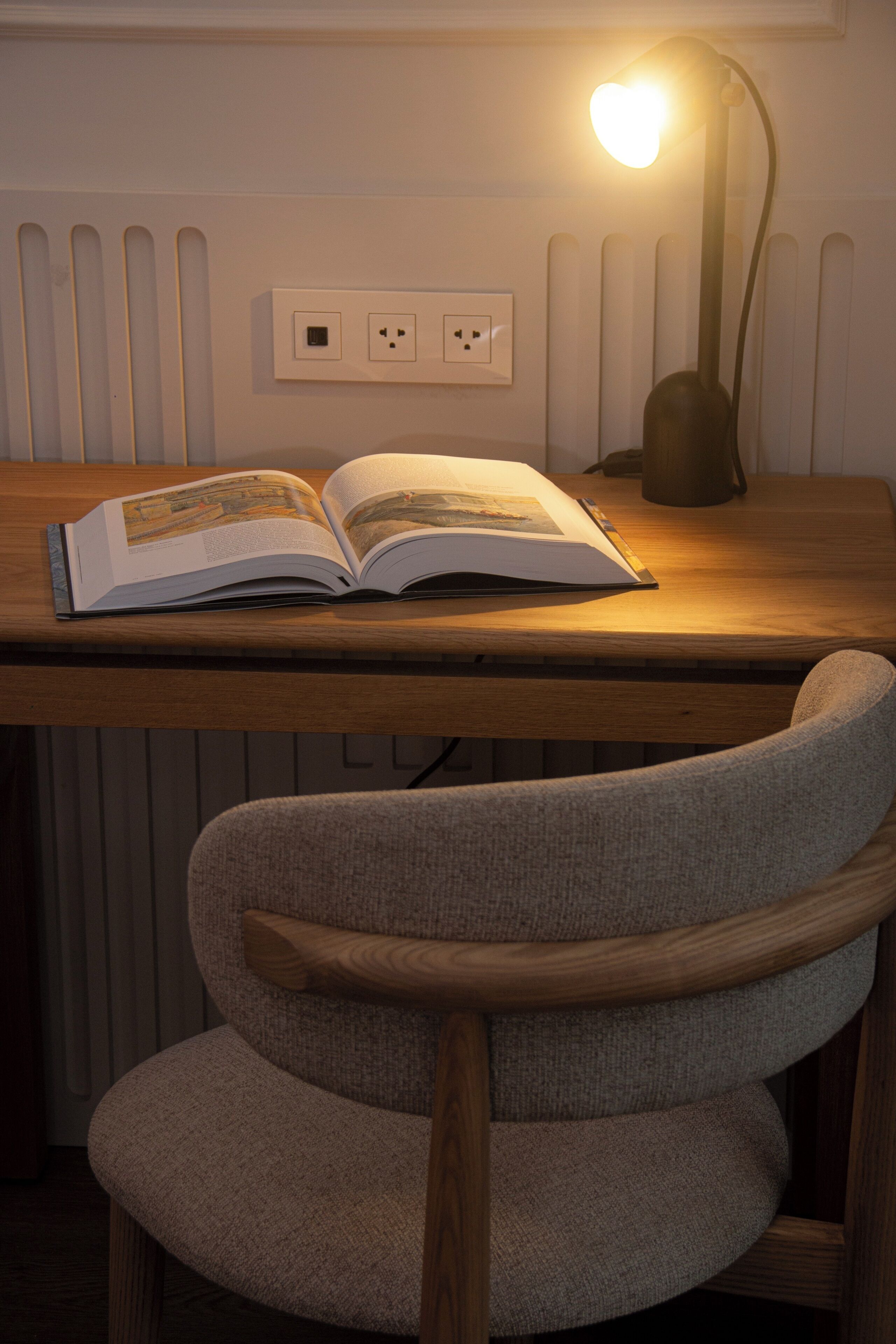 A wooden desk with an open book, a lamp, and a chair.