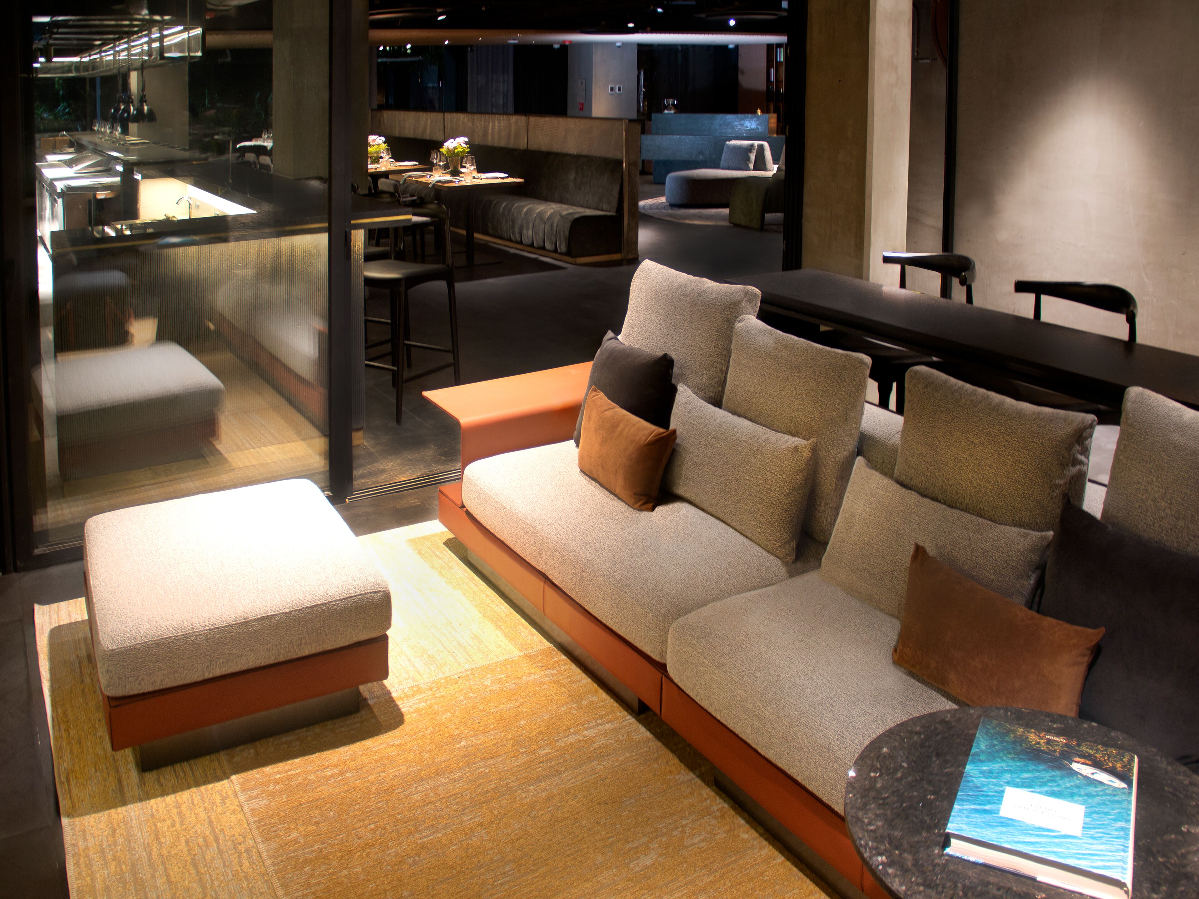 Ein modernes Interieur mit einer Couch, einem Hocker und einem kleinen Tisch mit einem Buch.