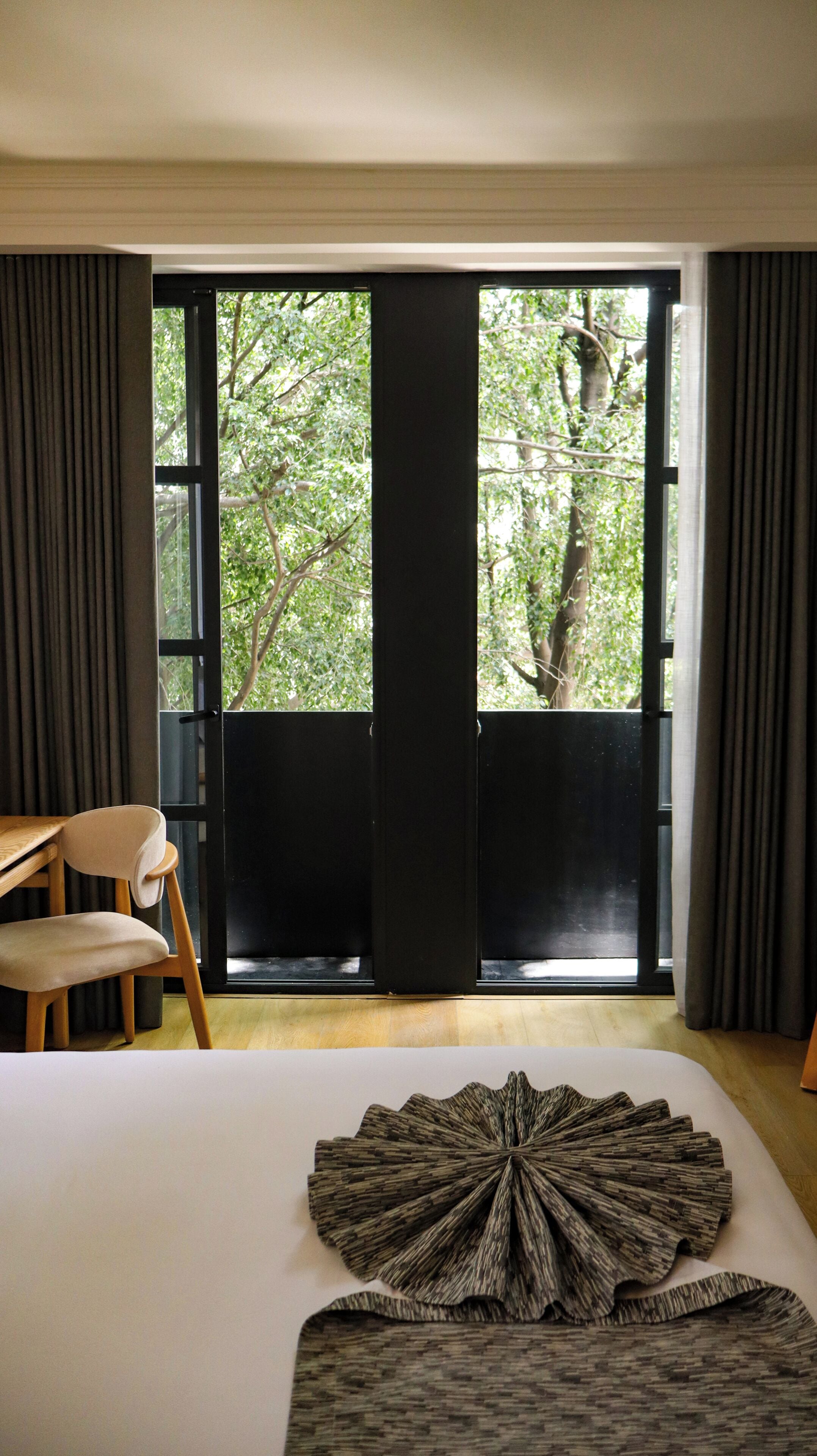 Un dormitorio con una ventana grande, una cama, una silla y vistas a árboles.