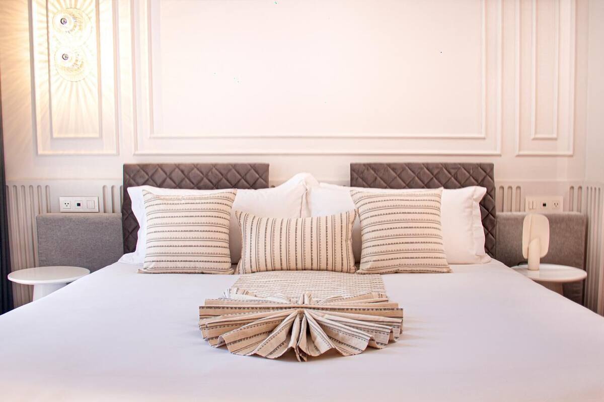 Cama bem arrumada com almofadas listradas, um cobertor dobrado e cabeceira com padrão de losangos.