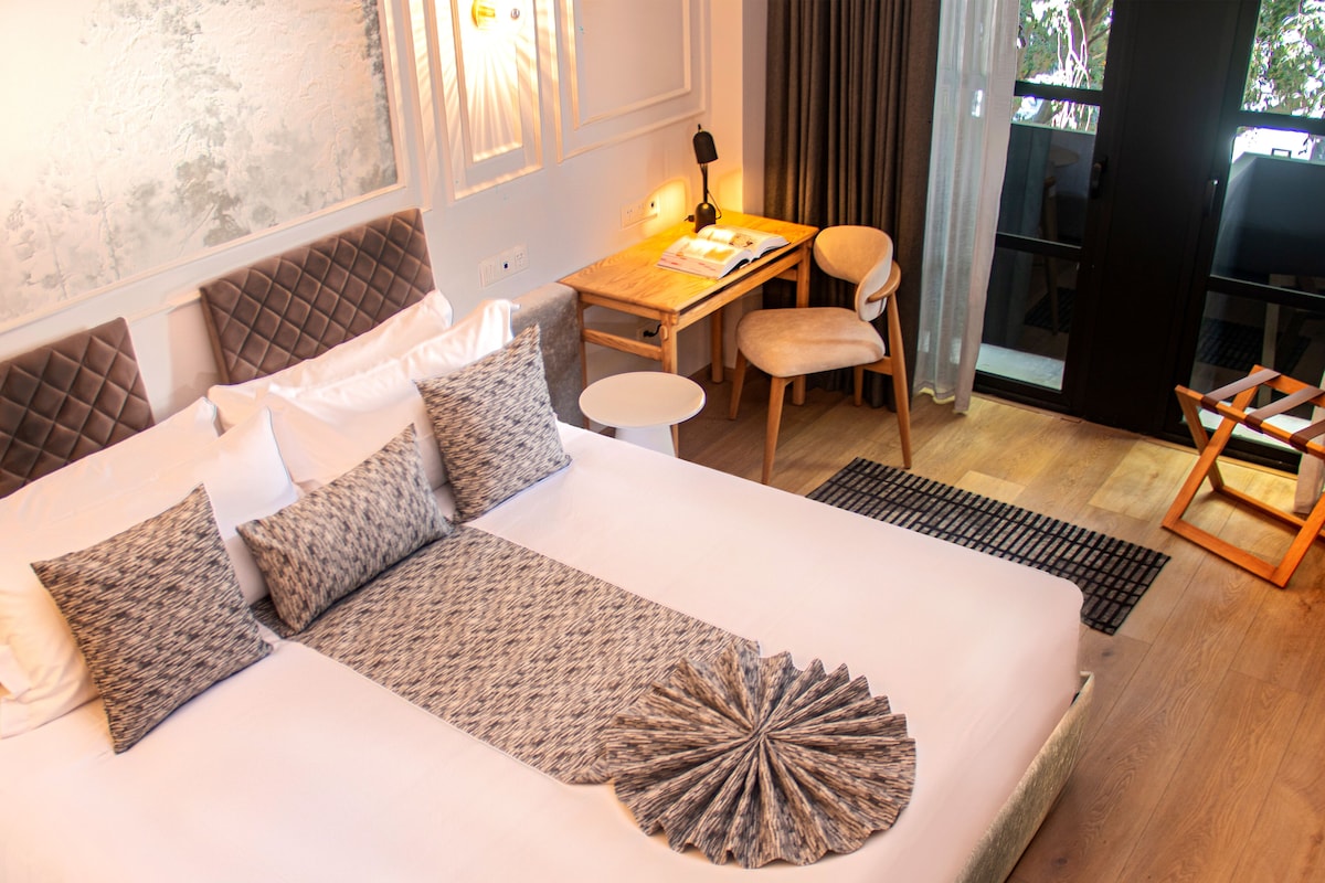 A hotel room with a large bed, a desk, a chair, and a view of the outdoors.
