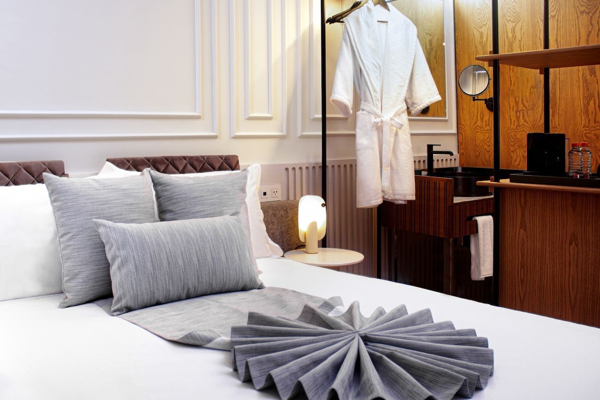 A neatly made bed with pillows, a bedside lamp, a wooden wardrobe, and a mirror.