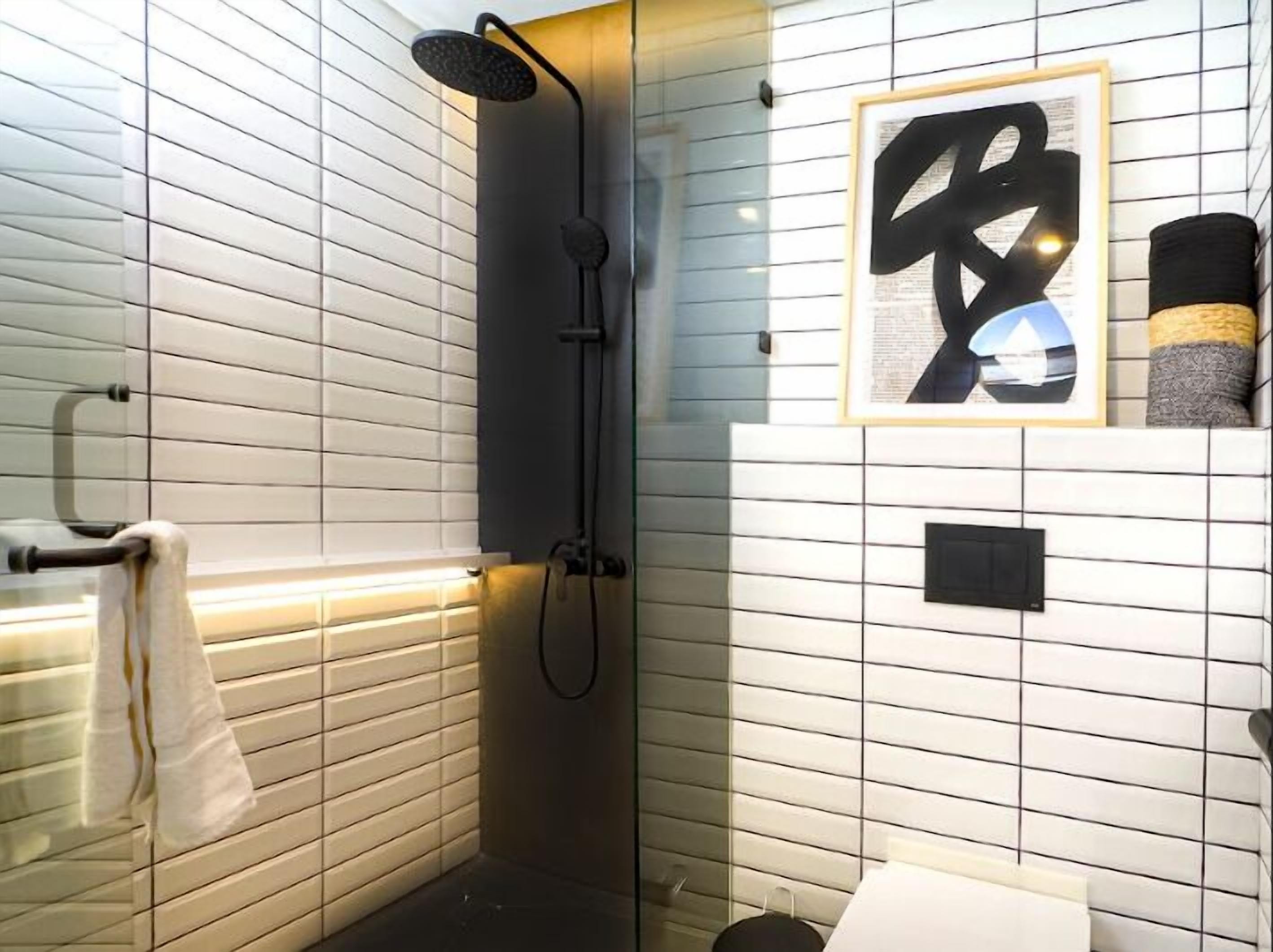 A bathroom with a shower, a towel rack, a framed artwork, and a toilet.
