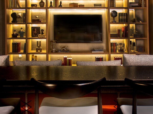 Een gezellige bar met een flatscreen televisie, boekenplanken en decoratieve items, plus comfortabele zitplaatsen.