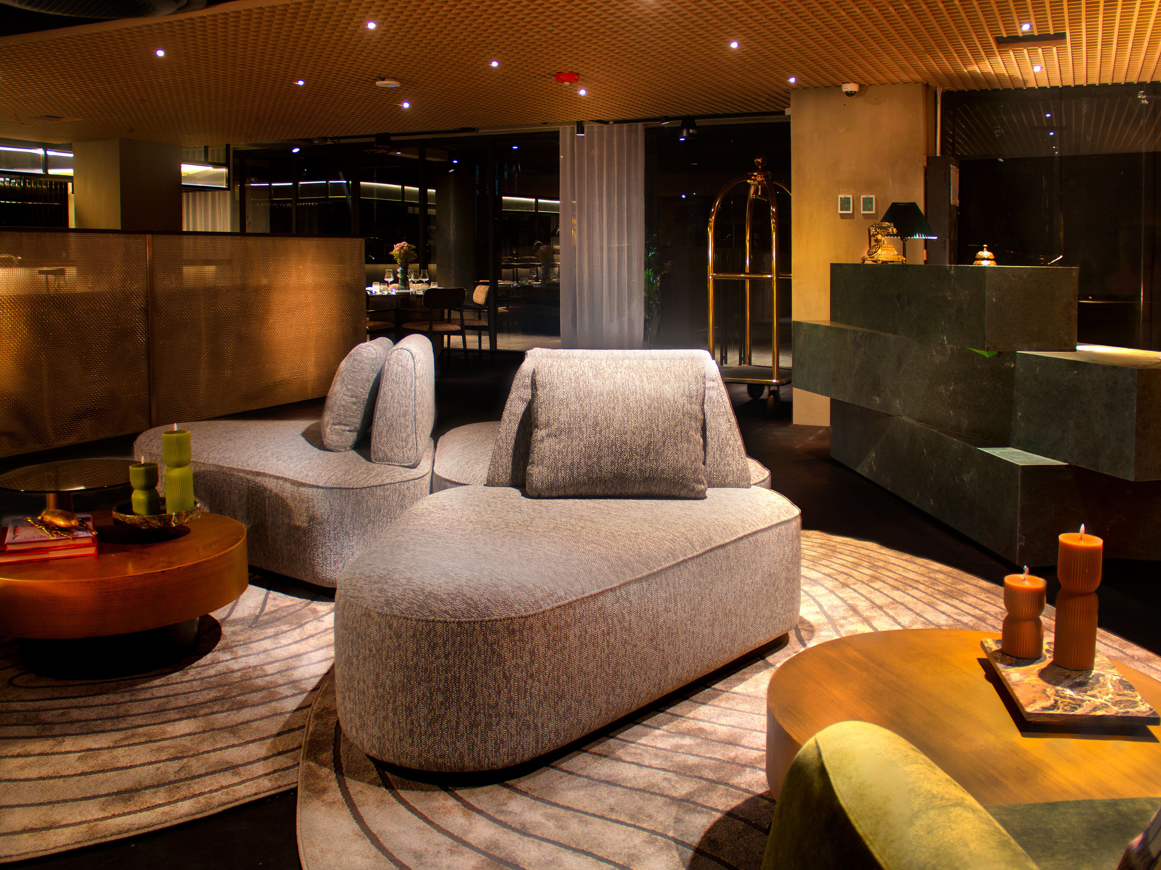 A modern hotel lobby with a sectional sofa, a round coffee table, and a reception desk.