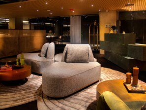 Eine moderne Hotelhalle mit Ecksofa, rundem Couchtisch und einer Rezeption.