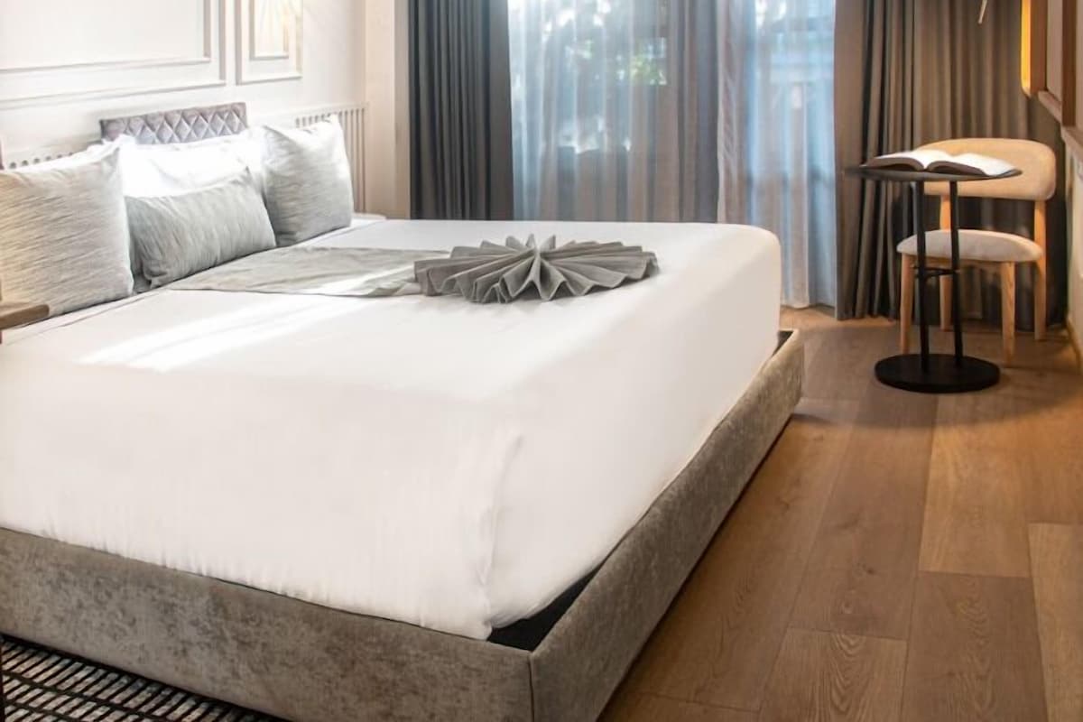 A neatly made bed with a grey headboard, a side table with a book, and a chair.