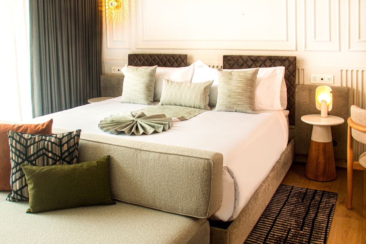 A neatly arranged hotel room with a bed, a sofa, a small table, and a lamp.