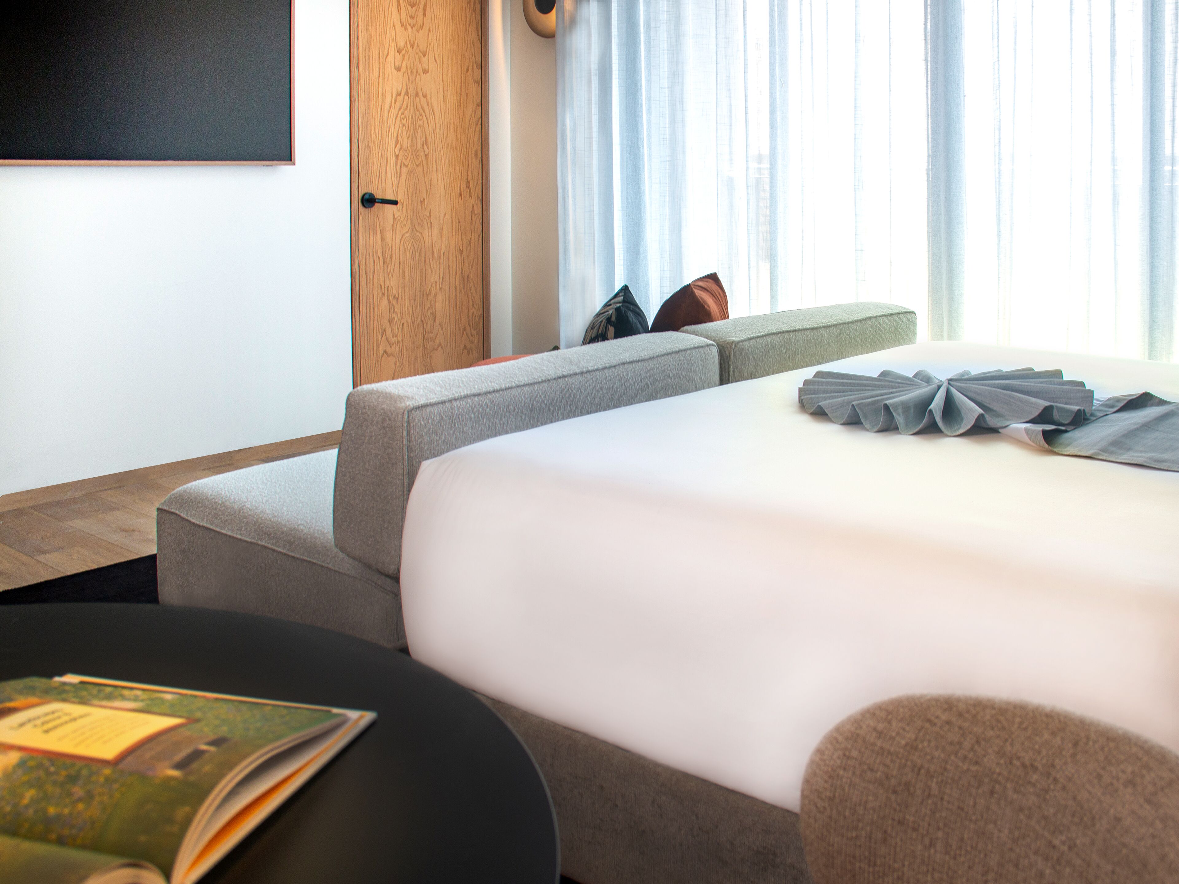 A hotel room with a bed, a sofa, a small table, and a TV on the wall.