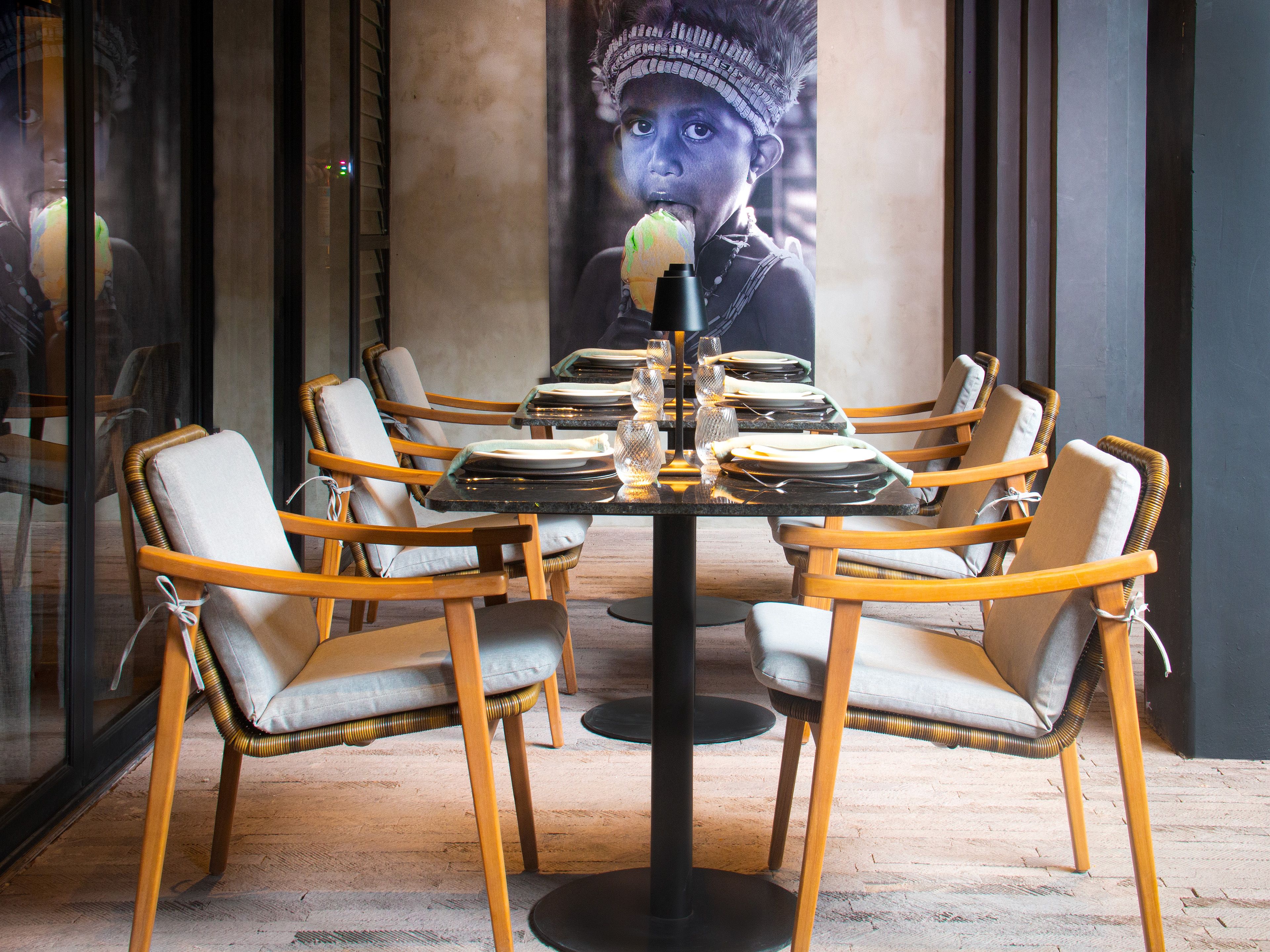 Un comedor con una mesa redonda dispuesta para seis personas, rodeado de sillas de mimbre con asientos acolchados.