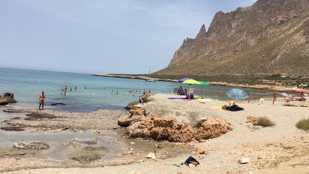 Une plage au paysage rocheux, avec une eau cristalline et une chaîne de montagnes en arrière-plan.