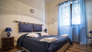 Une chambre à coucher avec un lit, deux tables de chevet, une commode, un rideau bleu et une chaise.