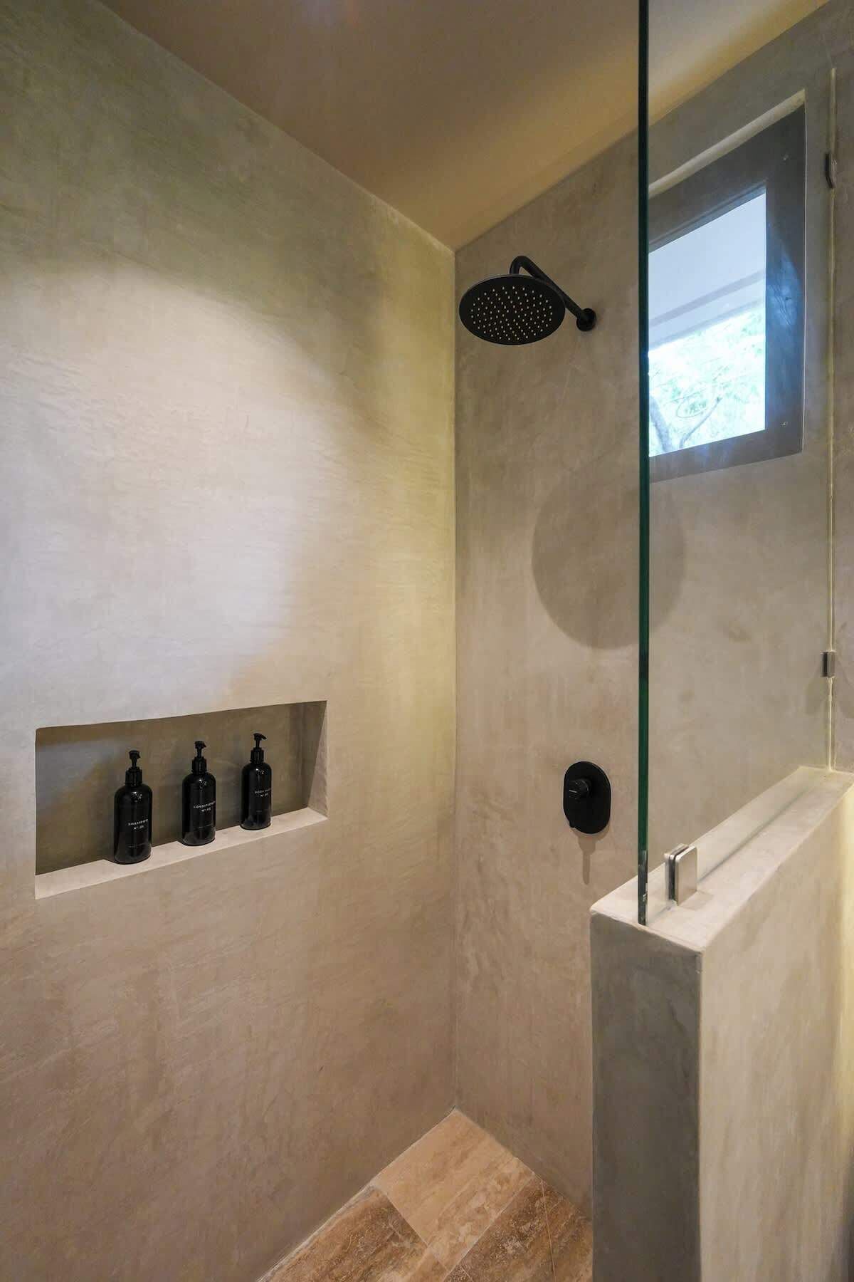 A modern bathroom with a shower, a window, and three black bottles on a shelf.