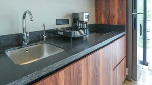 Moderni keittiö, jossa on tummat puukalusteet, ruostumattomasta teräksestä valmistettu allas ja kahvinkeitin.