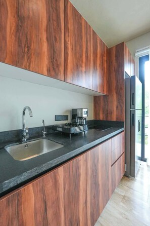 A modern kitchen with dark wood cabinets, a stainless steel sink, and a coffee machine. - Modern Studio Next to Holistika with Pool Views (Tulum)