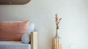 A modern bedroom with a minimalist design, featuring a sofa, a decorative vase, and a woven rug. - Executive Unit in Aldea Zama and Parking (Tulum)