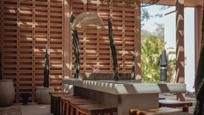 A bar area with wooden stools, a bar counter, and a decorative plant. - Executive Unit in Aldea Zama and Parking (Tulum)
