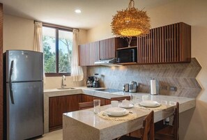 A modern kitchen with a built-in microwave, stainless steel refrigerator, and a dining area with a table set for two. - Tulum Getaway - 1BR with 2 Queen Beds & Pool (Tulum)