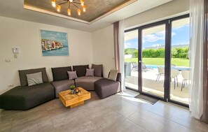 Ein Wohnzimmer mit Ecksofa, Couchtisch, einem Gemälde und einer Schiebetür zum Poolbereich.