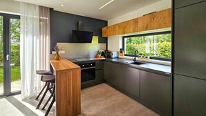 Een moderne keuken met een groot raam, donkere kastjes en een houten bar.