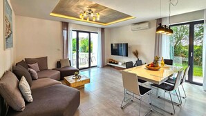 Een moderne woonkamer met een bank, eettafel, stoelen, een televisie en een groot raam met uitzicht.