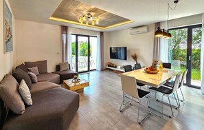 Ein modernes Wohnzimmer mit einer Couch, einem Esstisch, Stühlen, einem Fernseher und einem großen Fenster mit Blick.