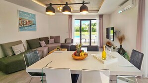 Een moderne woonkamer met een grote eettafel, een bank en een aan de muur bevestigde televisie.