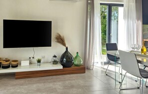A modern living room with a flat-screen TV, a wooden console table, decorative vases, and a dining area with a table and chairs. - Gorgeous home in Zminj (Zminj)