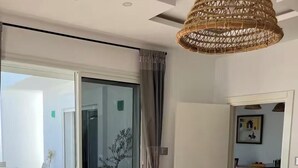 Une chambre moderne dotée d’une porte-fenêtre coulissante donnant sur un balcon, d’un luminaire au plafond en fibres tressées et d’un tapis à motifs sur le sol.