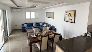 Un vaste espace de vie comprenant un coin repas avec une table pour quatre personnes, un canapé et un coin cuisine doté d’un plan de travail.
