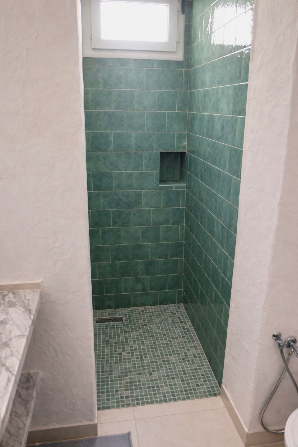 A bathroom with green tiles, a small window, and a shower area.