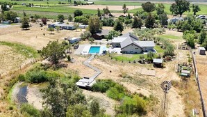 Una casa grande con piscina, rodeada de campos y un molino.