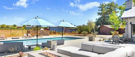 A backyard with a pool, outdoor seating, and umbrellas.