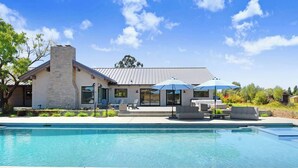 Una casa moderna con piscina, mobiliario de exterior y chimenea de piedra.